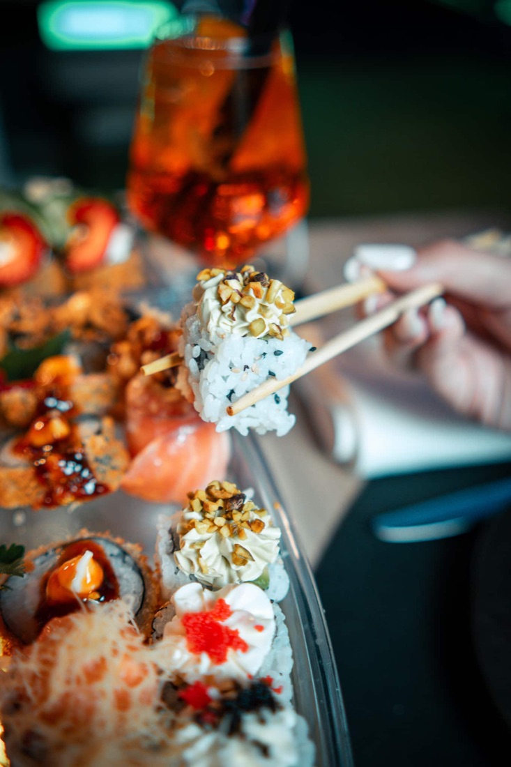 Uramaki sollevato con le bacchette sopra un plateau di sushi del Live